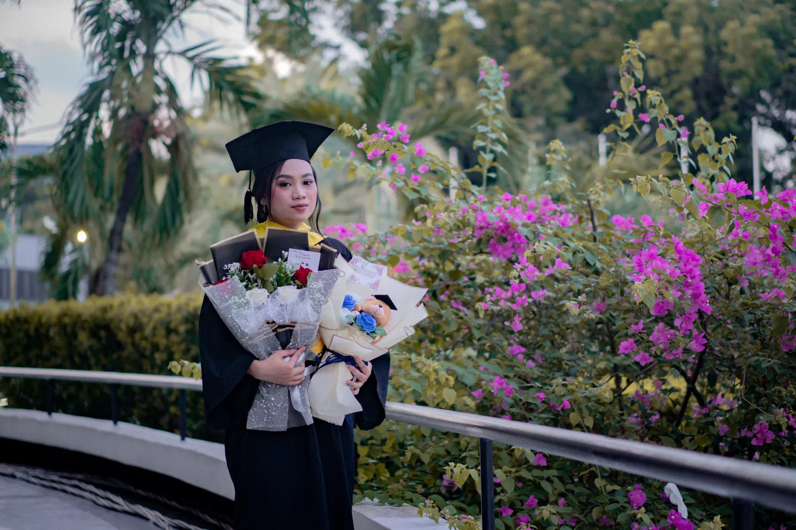 Wisudawati memegang buket bunga di taman berbunga ungu