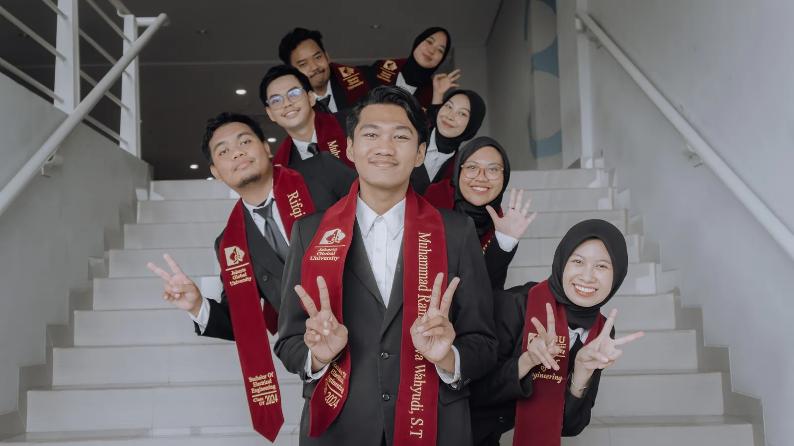 Wisudawan dan wisudawati berpose peace di tangga kampus